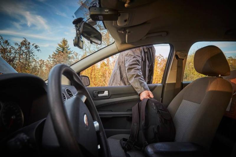 Image of a man stealing a bag from a parked car. 