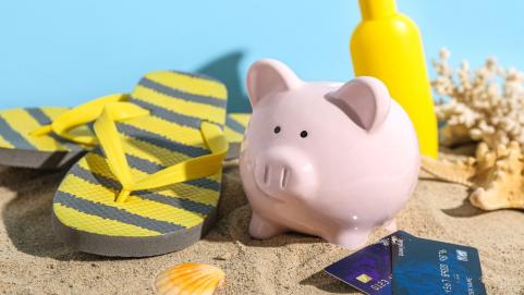 Piggy bank with beach accessories, sunscreen cream and credit cards on sand 